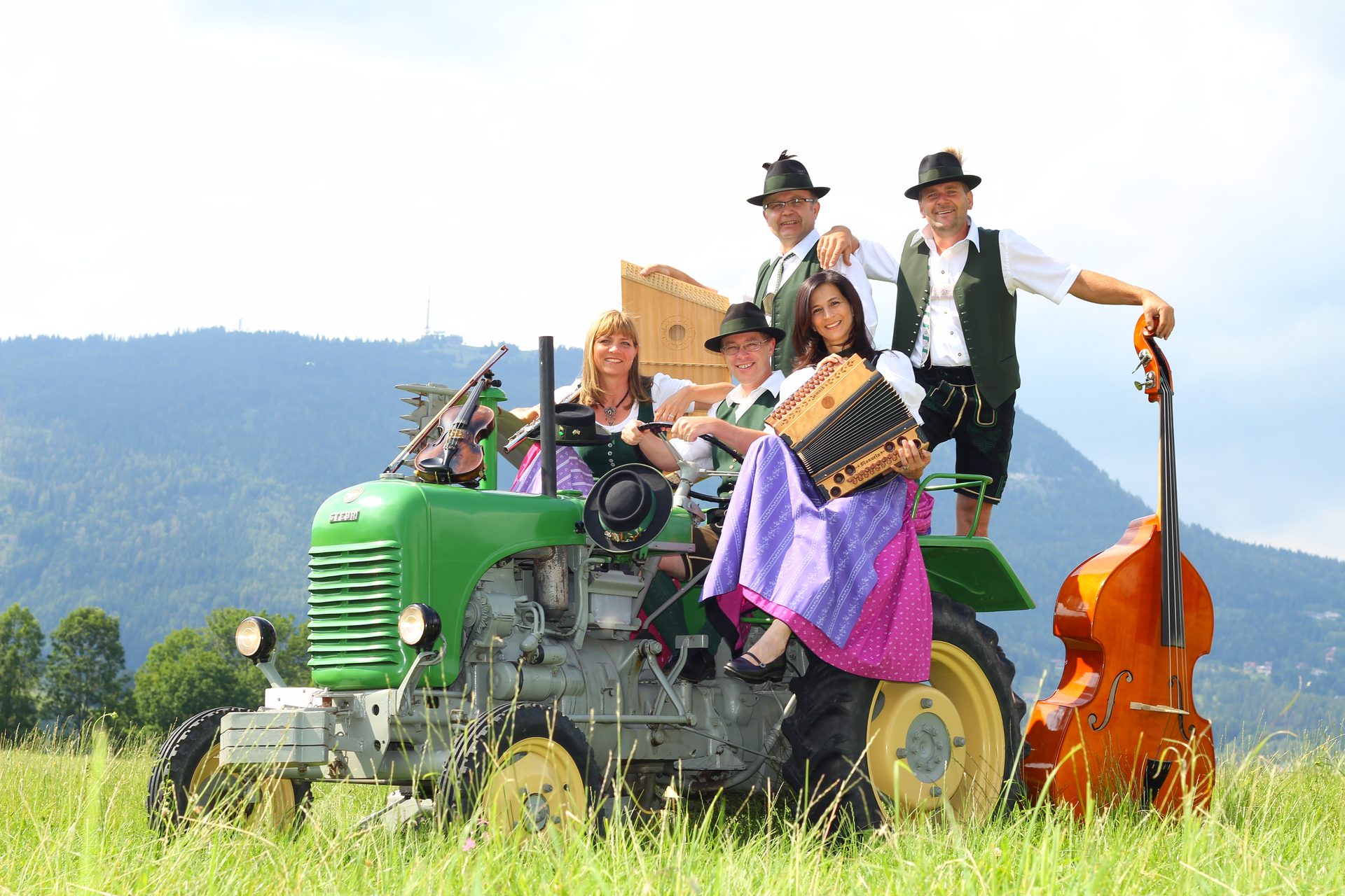 Knöpferlstreich mit Instrumenten auf einem grünen Steyr-Traktor in der Almwiese